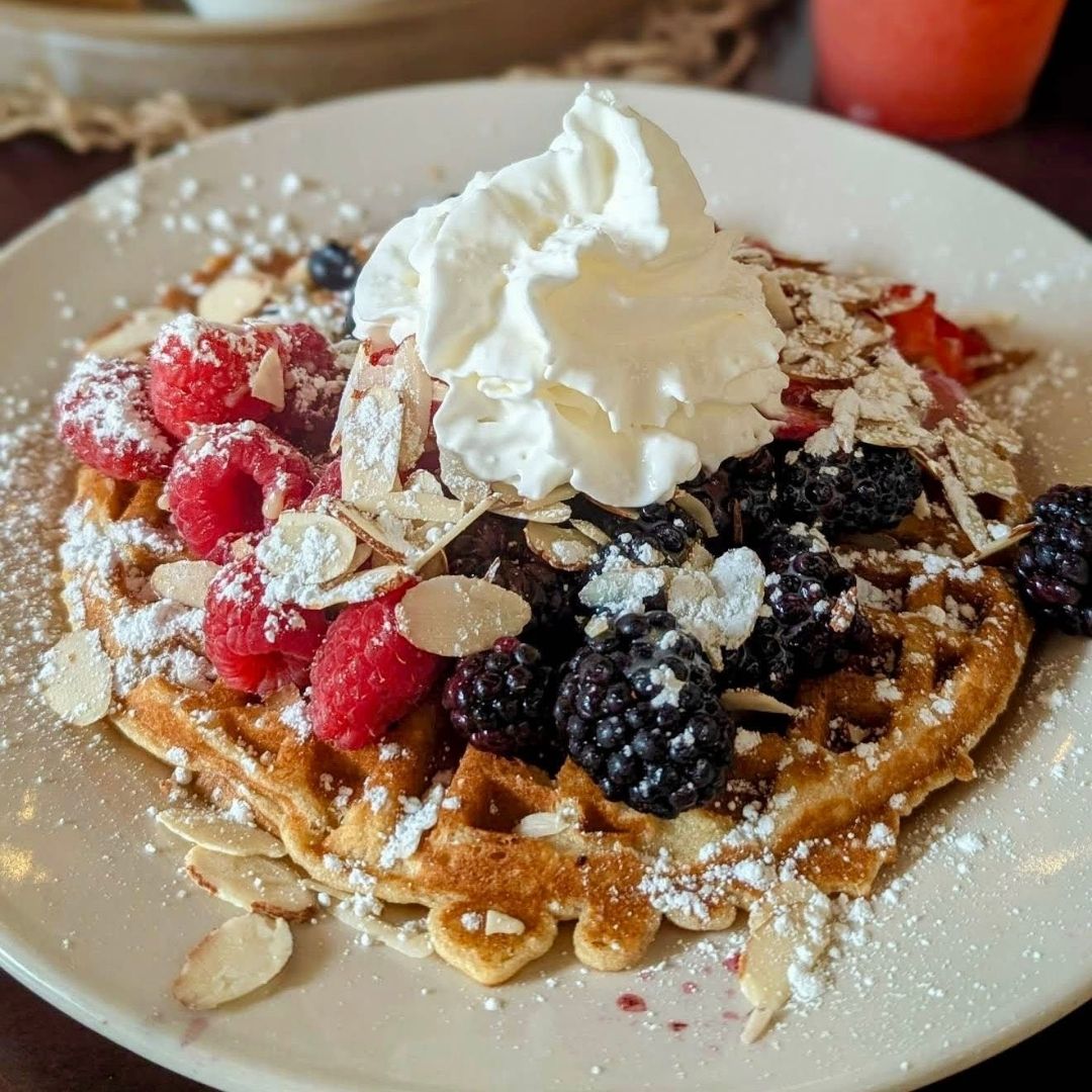 A warm gluten-free waffle topped with fresh berries and whipped cream.